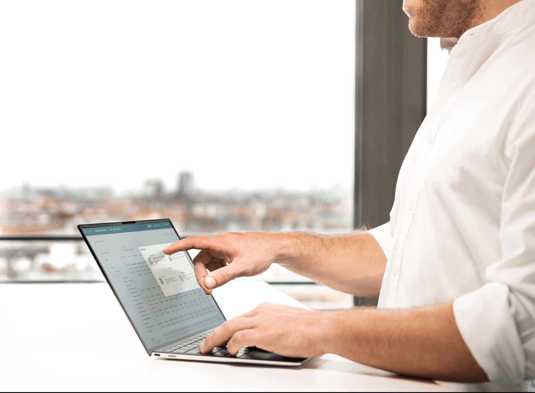 Man tapping a laptop showing Fairmas cashflow software, with a blurred city skyline behind him.